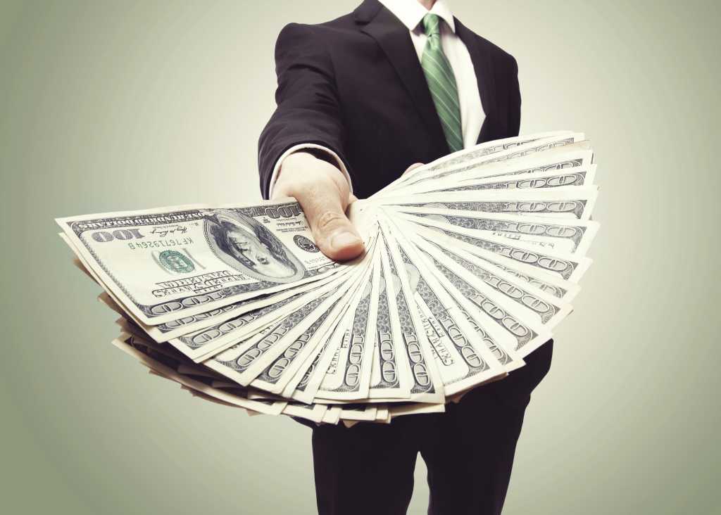 man in suit holding out huge fan of money